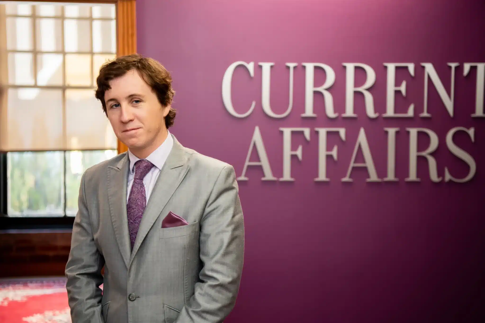 Nathan J. Robinson Standing Next to a Current Affairs Banner