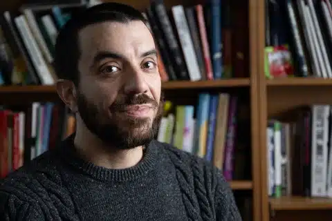 Kaveh Akbar Smiling With Books in the Background