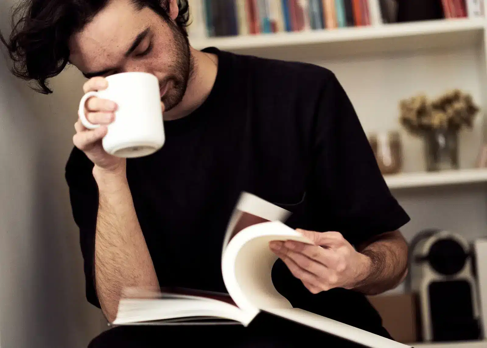 A Young Man Reading a Book and Holding a Mug