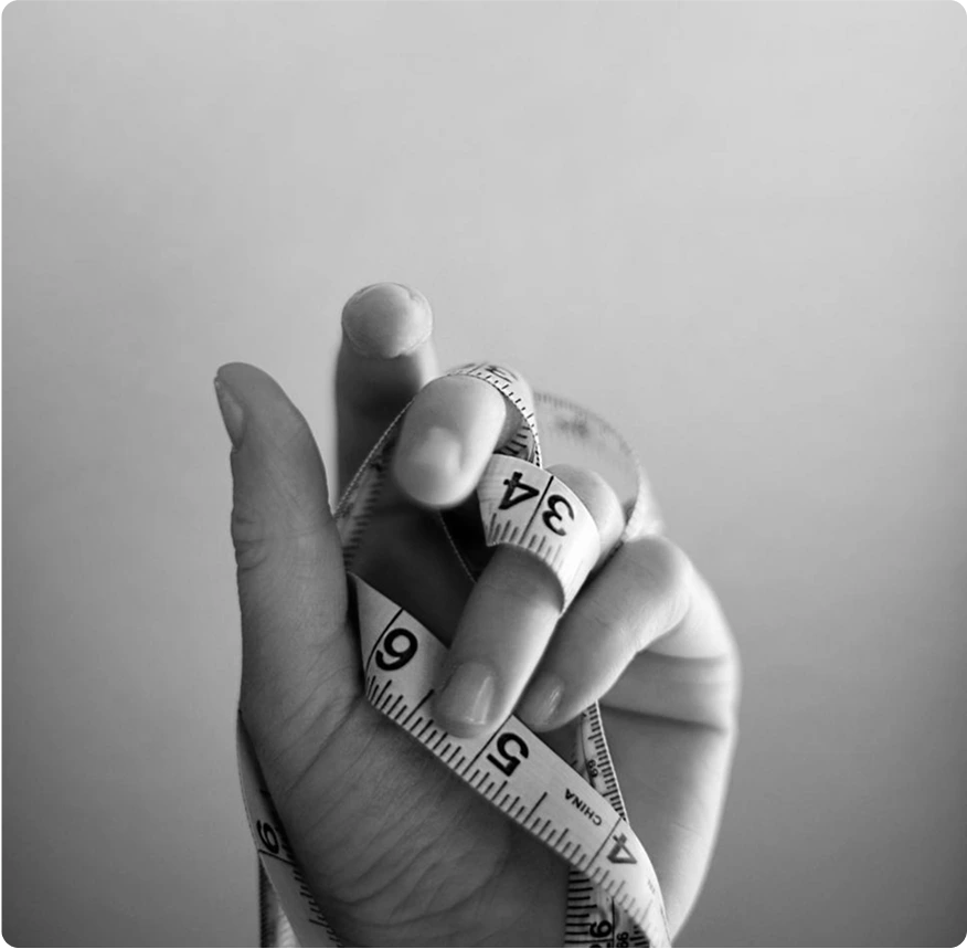 A hand with a tape measure woven between the fingers.